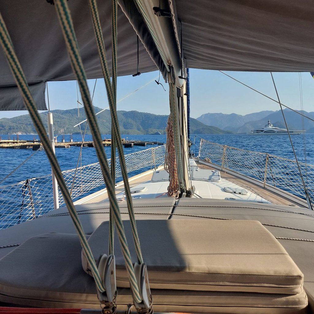 Yelkenli teknenin güvertesinde yastıklar ve ipler, deniz ve uzakta dağlar.