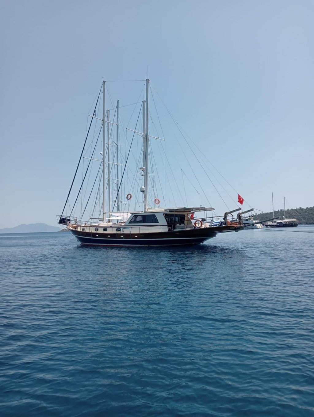 Mavi denizde, yelken direkleri ve Türk bayrağı olan gulet tipi yelkenli tekne.