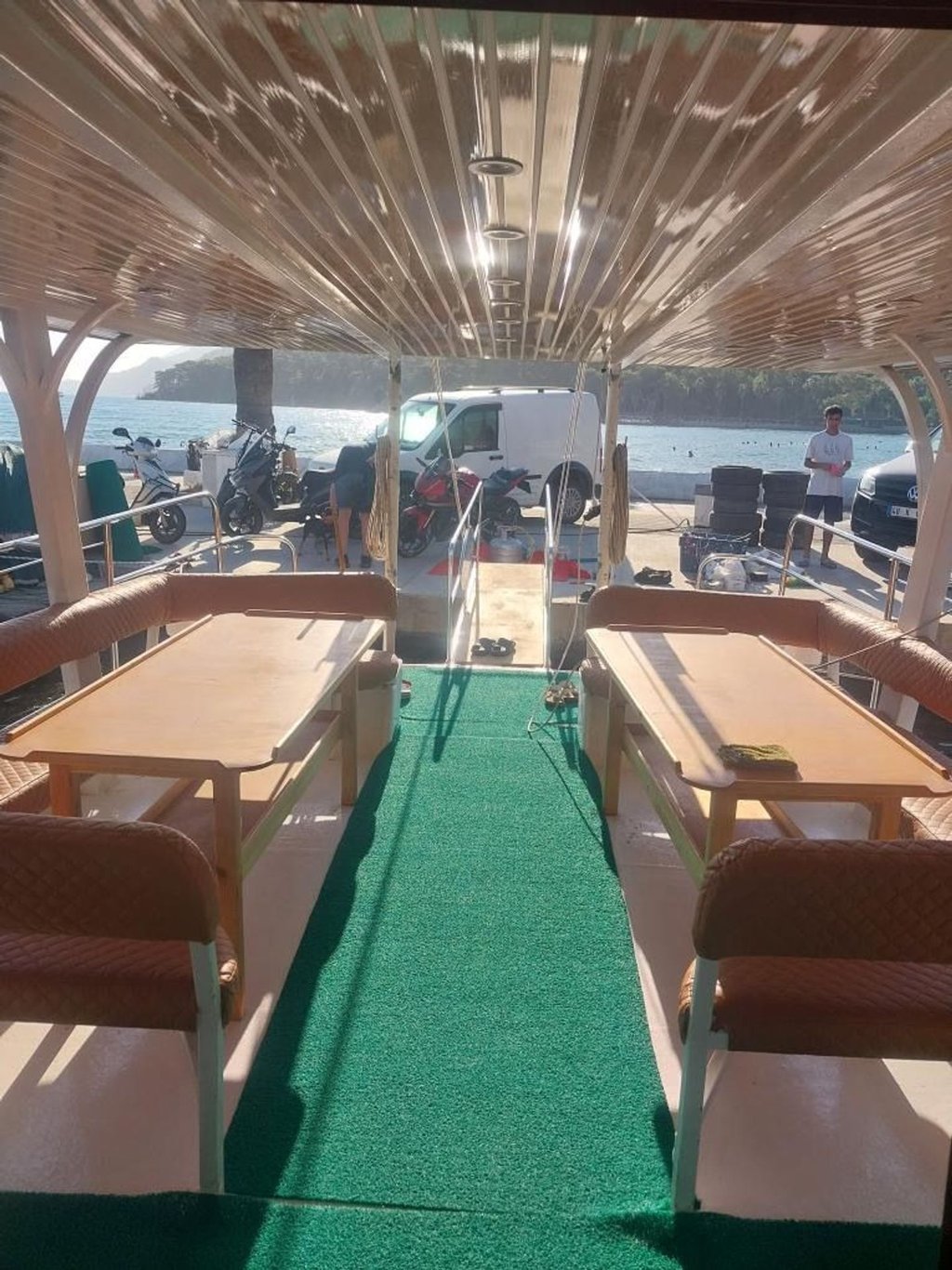 Ahşap tavanlı teknede, yeşil halı ve iki yanındaki masalar ile sandalyeler.