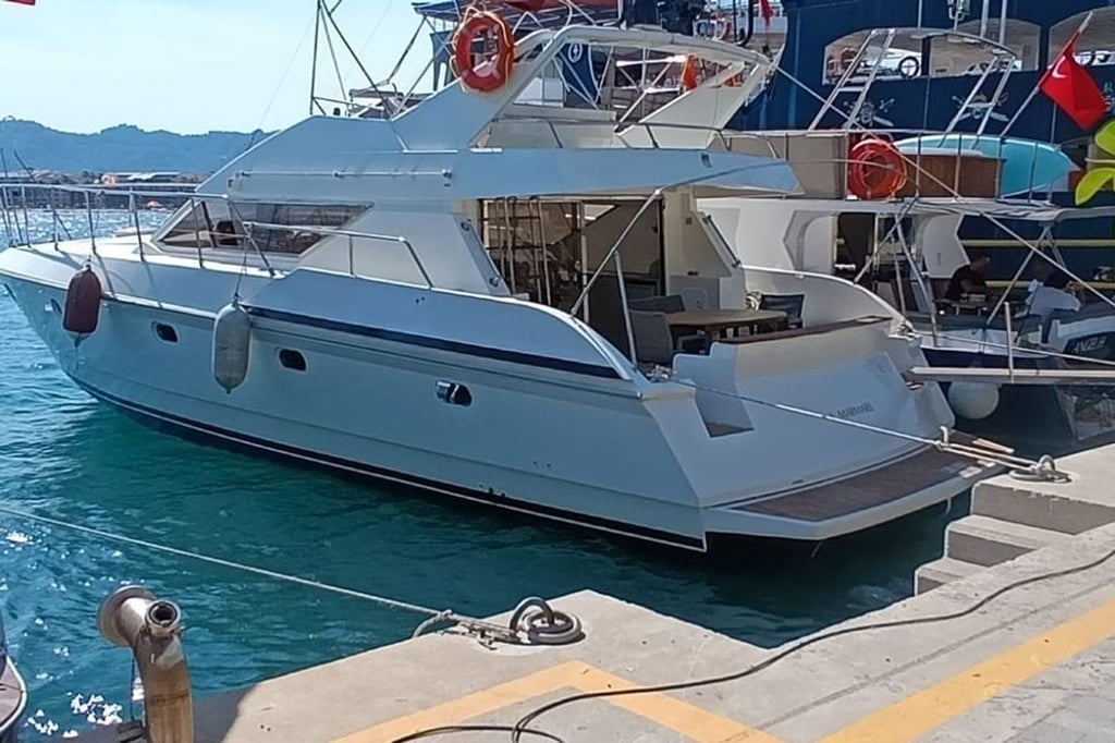 Mavi suda, iskeleye bağlı beyaz motor yat ve arka kısmında oturma alanı.