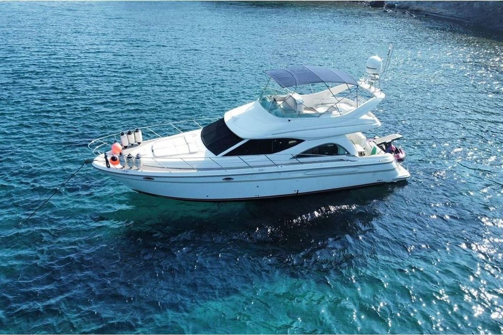 Mavi denizde, beyaz ve modern bir motor yat, üstünde tente ve antenler.