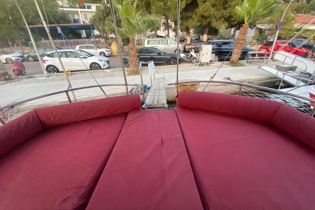 Bordo yastıklarla kaplı geniş yatak alanı ve iskeleye bağlanan tekne güvertesi.