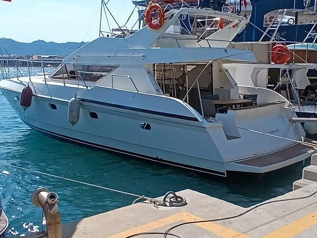 Mavi suda, iskeleye bağlı beyaz motor yat ve arka kısmında oturma alanı.