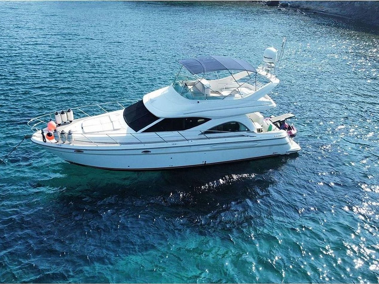 Mavi denizde, beyaz ve modern bir motor yat, üstünde tente ve antenler.