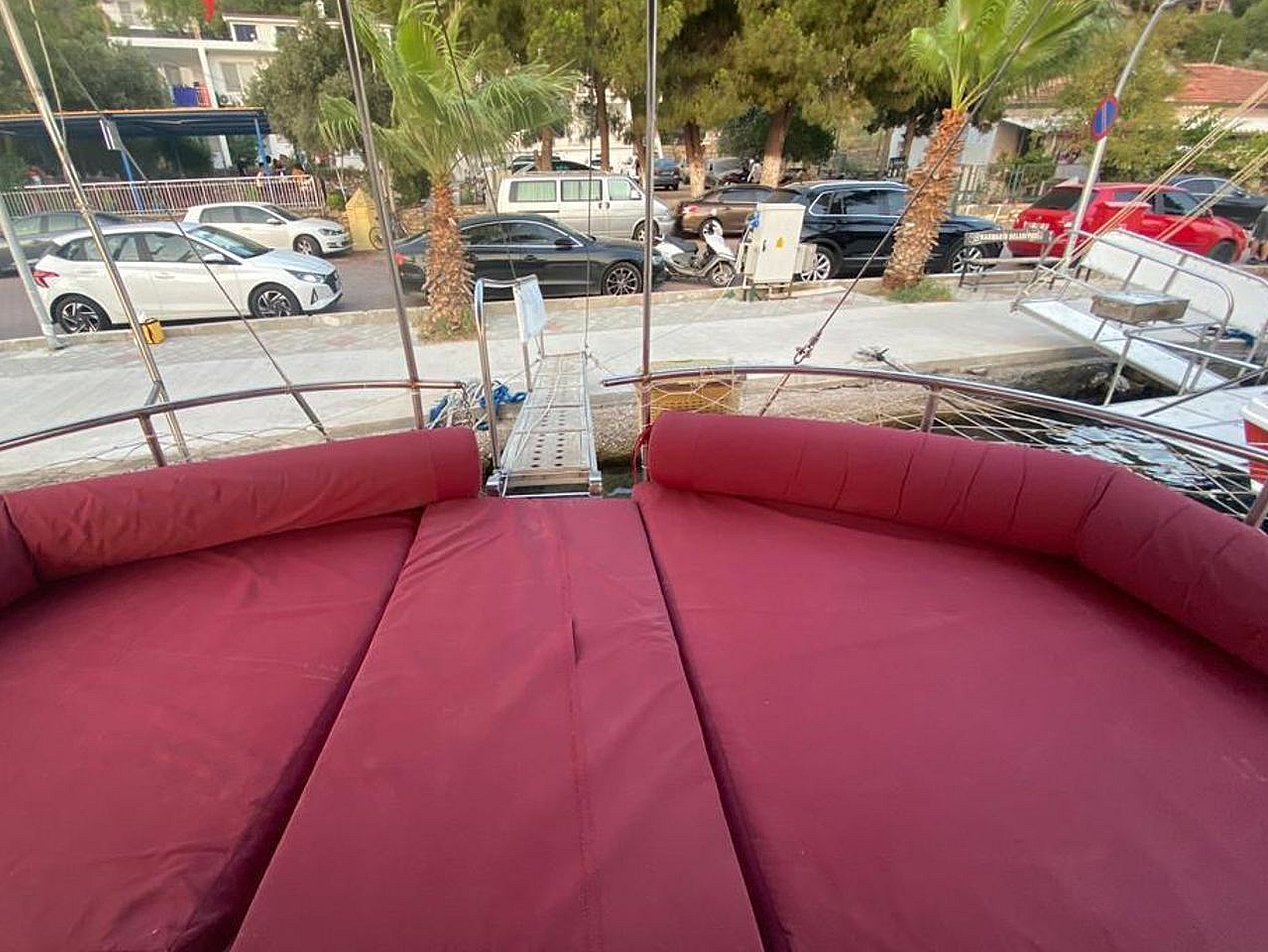 Bordo yastıklarla kaplı geniş yatak alanı ve iskeleye bağlanan tekne güvertesi.
