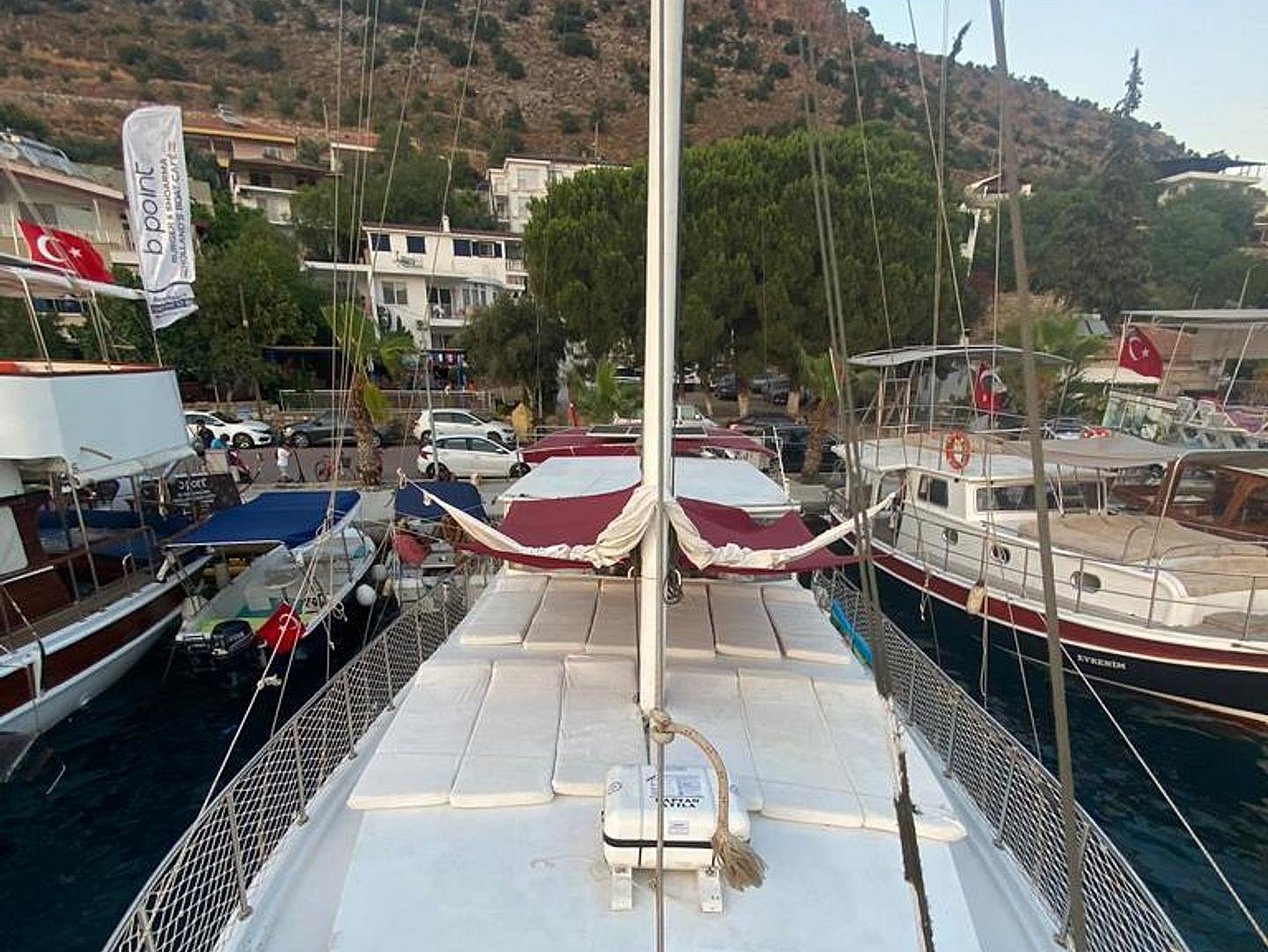 Beyaz güvertesi ve direği olan yelkenli tekne, limanda diğer teknelerin arasında demirli.