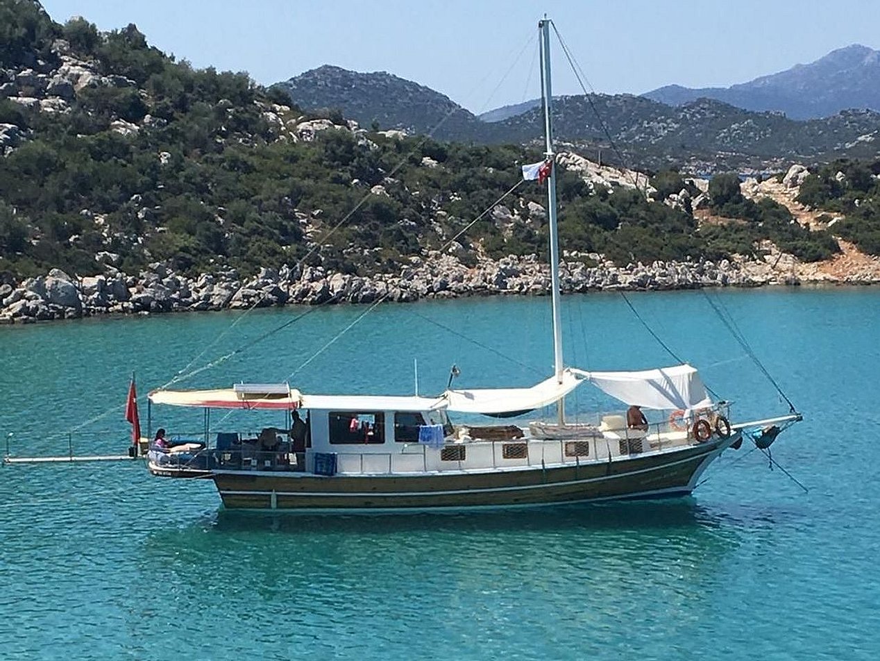 Mavi suda, arka kısmında kırmızı bayrak ve beyaz tente bulunan yelkenli tekne.