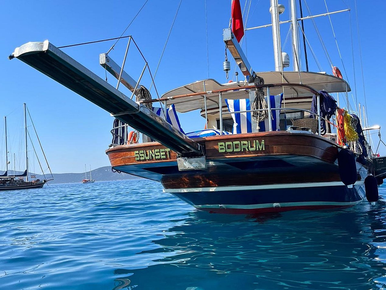 Mavi suda, arka kısmı ve Türk bayrağı görünen gulet yat.