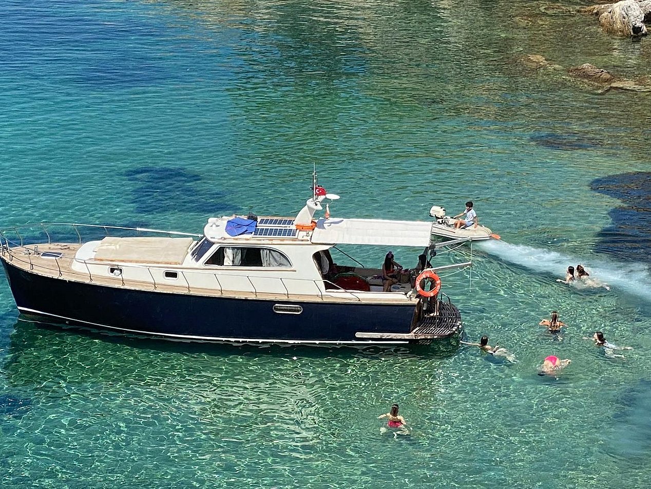 Mavi ve yeşil tonlarında berrak suda, üstü kapalı küçük tekne ve çevresinde yüzen insanlar.