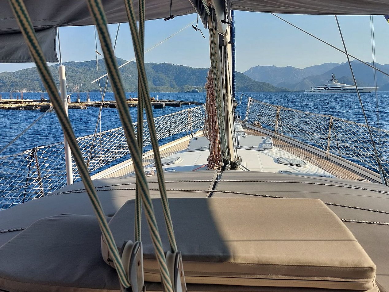 Yelkenli teknenin güvertesinde yastıklar ve ipler, deniz ve uzakta dağlar.