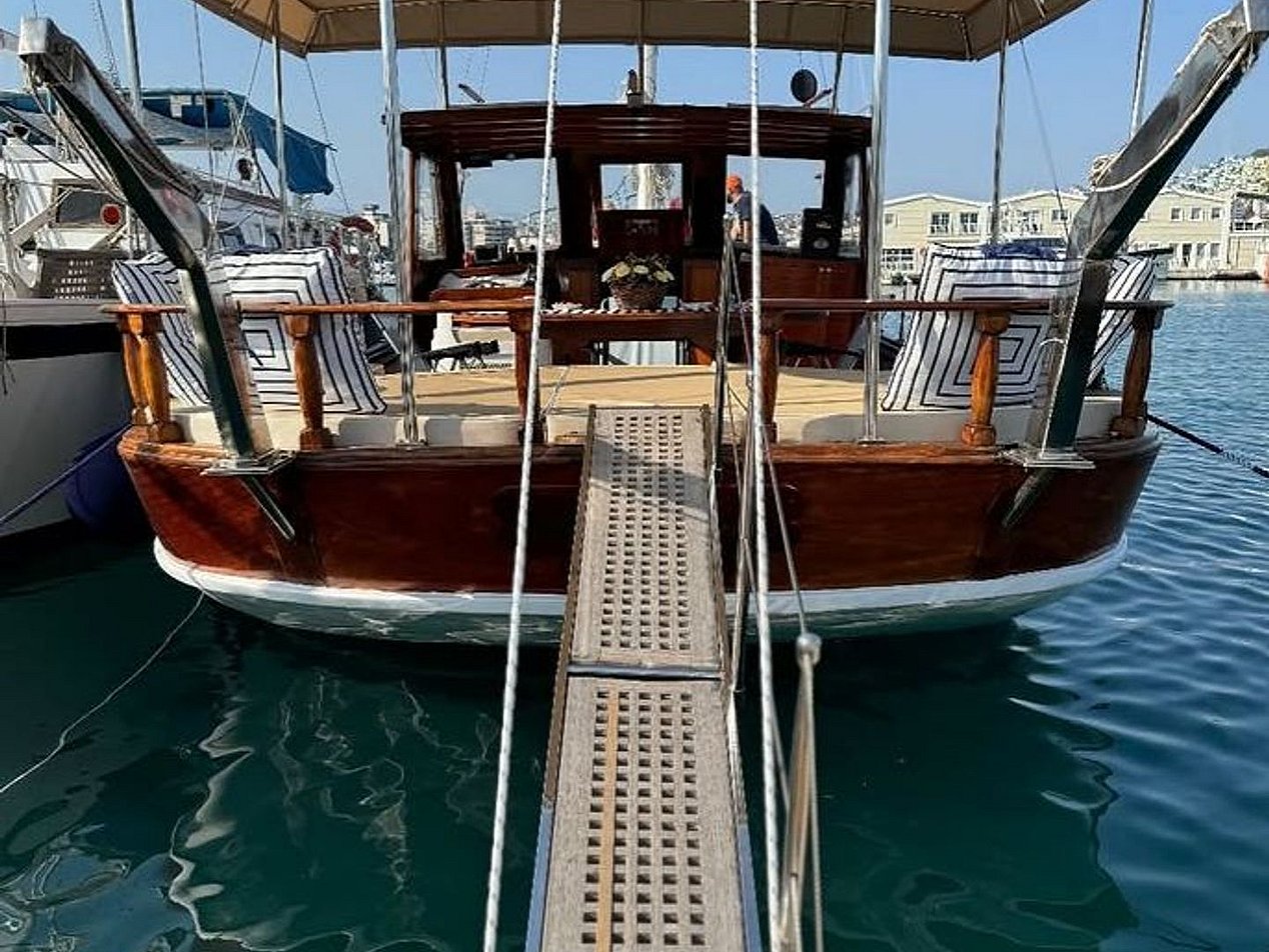 Ahşap iskeleye bağlı, bej tente kaplamalı, minderli oturma alanı olan ahşap tekne.