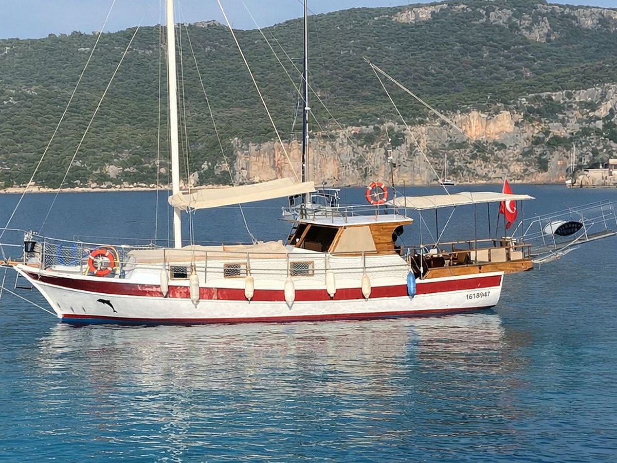 Denizde, beyaz ve kırmızı renkli yelkenli tekne, arka kısmında Türk bayrağı ve can simidi.