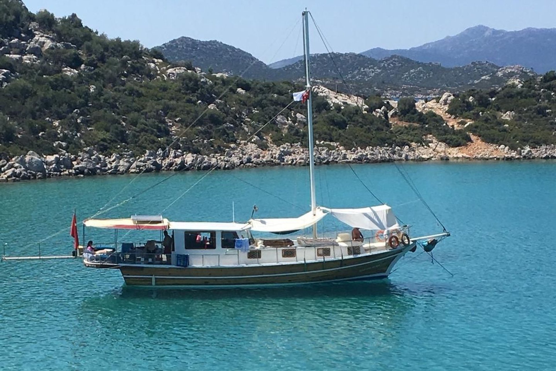 Mavi suda, arka kısmında kırmızı bayrak ve beyaz tente bulunan yelkenli tekne.